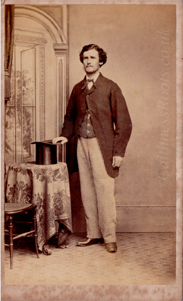 Victorian gentleman standing in front of a painted backdrop, holding a top hat